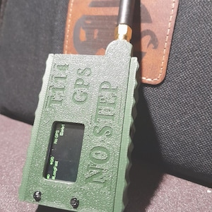 May include: A green GPS device with the text "TILT GPS NO STEP" and a small screen displaying data. It has a black antenna and is attached to a brown leather patch. The device is secured with black screws.