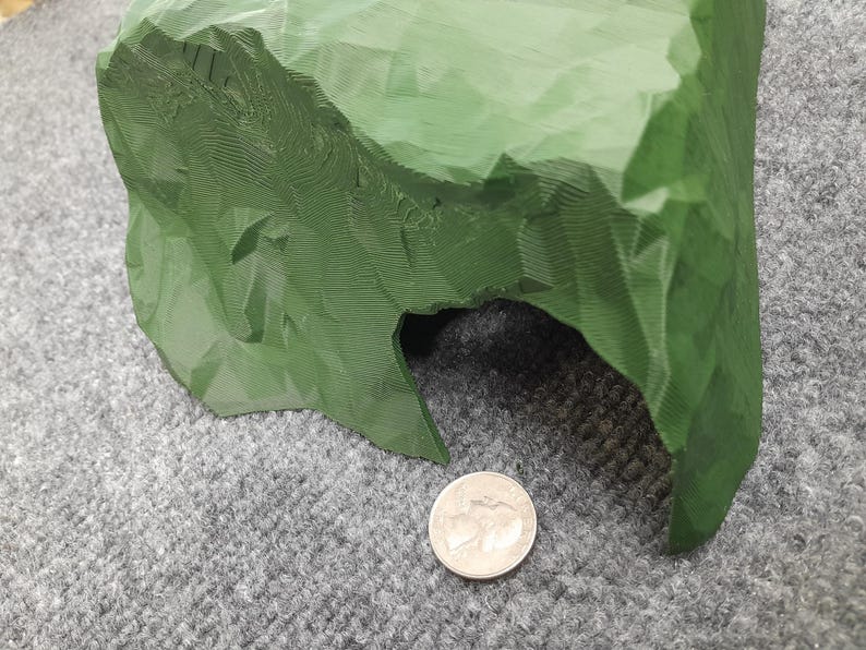 Pode incluir: Uma caverna verde impressa em 3D com uma superf&iacute;cie texturizada e uma pequena abertura. A caverna est&aacute; sobre uma superf&iacute;cie cinza.