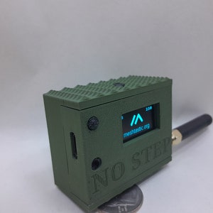 May include: A green, 3D printed box with a small screen displaying a blue arrow and the text "meshtastic.org". The box has a black antenna and the text "NO STEP" printed on the side.