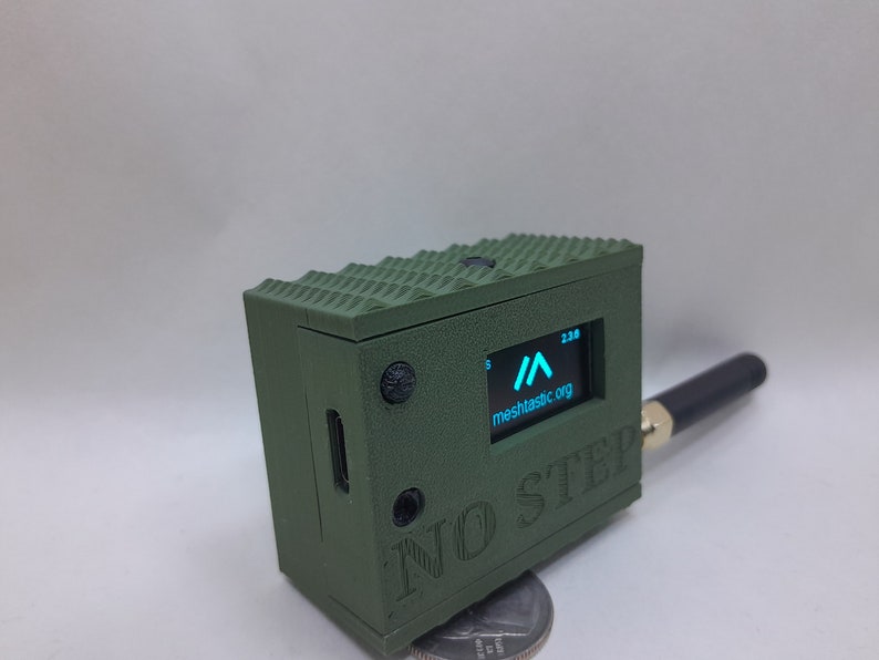 May include: A green, 3D printed box with a small screen displaying a blue arrow and the text "meshtastic.org". The box has a black antenna and the text "NO STEP" printed on the side.