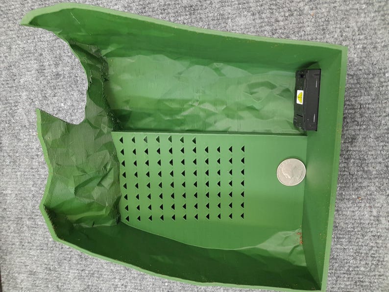 Pode incluir: Um recipiente de pl&aacute;stico verde com um inserto de padr&atilde;o triangular e um pequeno dispositivo eletr&ocirc;nico preto. O recipiente tem uma aba que pode ser levantada para acessar o interior.