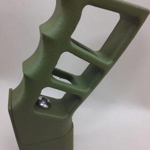 May include: A green 3D printed pistol grip with a textured surface and a silver screw.