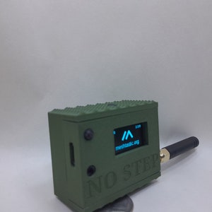 May include: A green, rectangular box with a small screen displaying a blue arrow and the text "mechcastic.org". The box has a black antenna and the text "NO STEP" printed on the front.