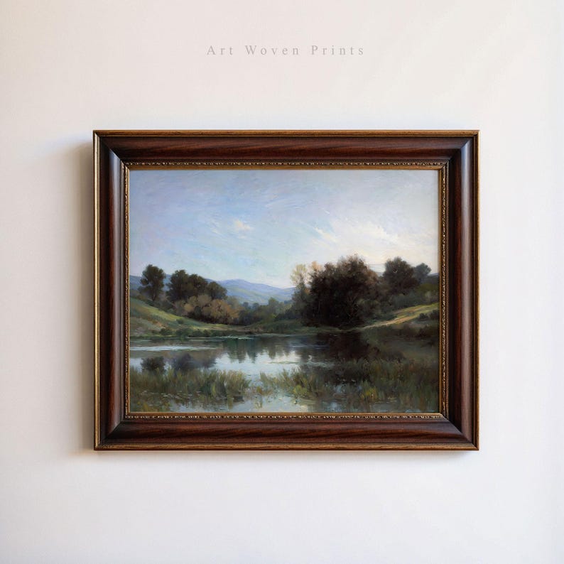 May include: A framed painting of a landscape with a lake in the foreground, surrounded by trees and hills. The sky is blue with white clouds. The painting is in a brown wooden frame.
