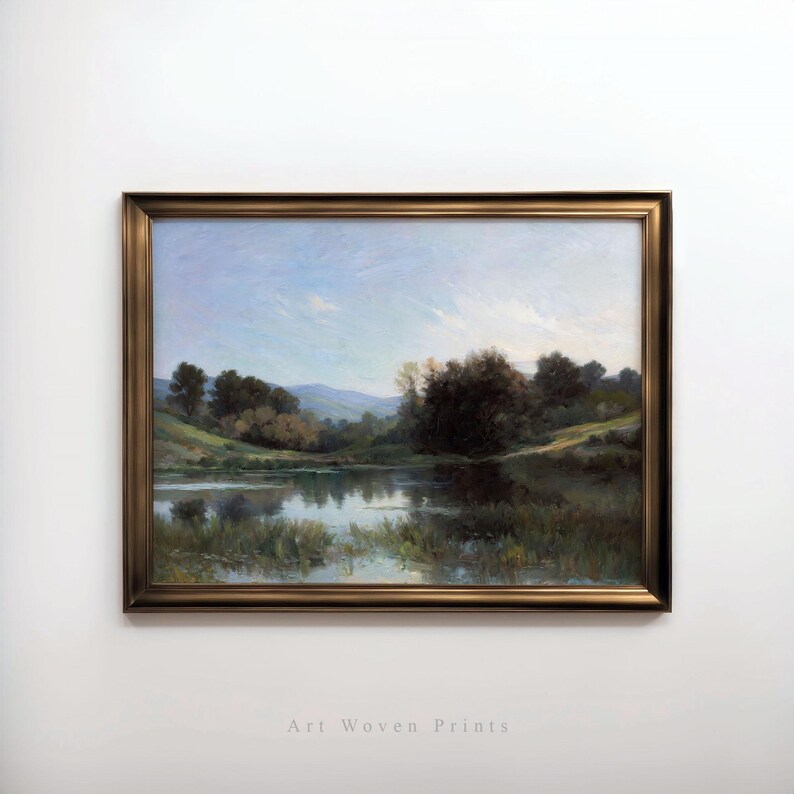May include: A framed landscape painting depicting a lake surrounded by trees and hills. The sky is a light blue with some clouds. The water is a calm blue with reflections of the trees and sky. The trees are a mix of green and brown.