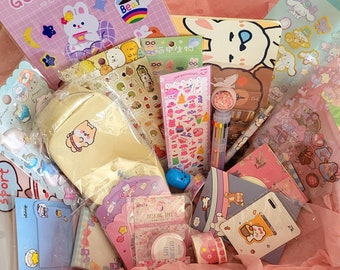 May include: A pink and white gift box filled with stationery and craft supplies. The box contains stickers, washi tape, notepads, and other items. The items feature a cartoon bear and other cute designs.