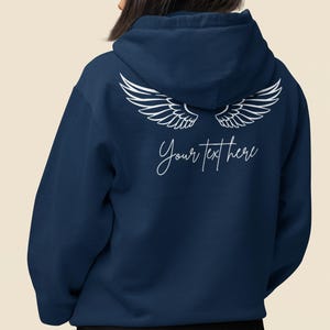 May include: Navy blue hoodie with white angel wings graphic on the back. The hoodie features the text "Your text here" in a cursive font. The garment is made of a soft material and has a hood.