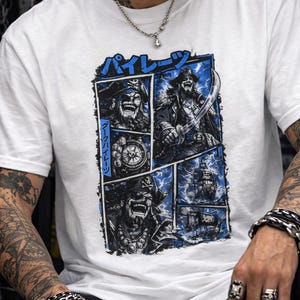 May include: White t-shirt featuring a blue and black comic-style graphic with pirate illustrations and Japanese text. The design includes images of pirates, a ship, and a compass. The shirt is made of a soft material.