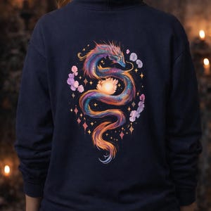 Peut inclure: Sweat à capuche bleu marine avec un motif de dragon coloré dans le dos. Le dragon est représenté avec un arc-en-ciel de couleurs, entouré d'éléments floraux et d'étoiles scintillantes. Le sweat à capuche a une capuche et des manches longues.