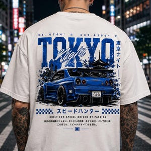 May include: A white t-shirt featuring a blue graphic on the back. The design displays a blue sports car, the text "TOKYO Night", Japanese characters, and the phrase "BUILT FOR SPEED. DRIVEN BY PASSION." along with coordinates and a checkered pattern.