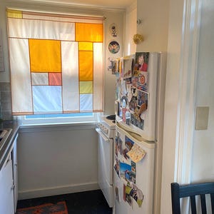 Puede incluir: Un refrigerador blanco con una estufa y horno negros. El refrigerador tiene una variedad de fotos y postales pegadas a la puerta. La cocina tiene un piso de baldosas blancas y una alfombra estampada.