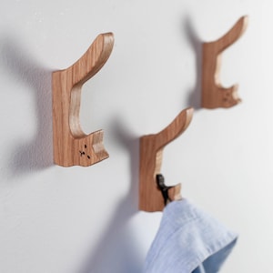Könnte beinhalten: Drei Wandhaken aus Holz in Katzenform, an einem der Haken hängt ein blaues Hemd.