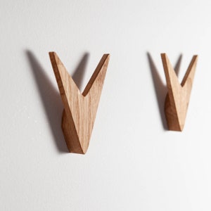 Könnte beinhalten: Zwei V-förmige Wandhaken aus Holz, die an einer weißen Wand befestigt sind.