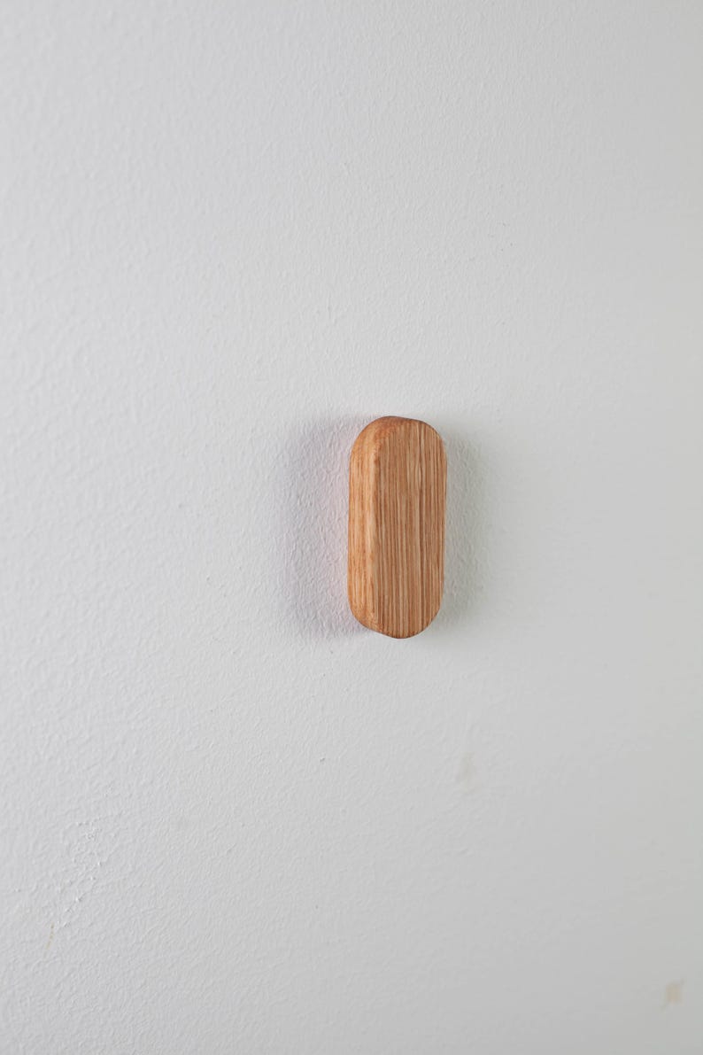 May include: A wooden hook in the shape of an oval, mounted on a white wall.