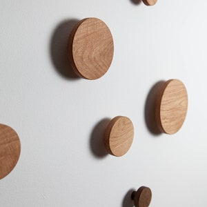 May include: Five wooden wall hooks in various sizes, mounted on a white wall. The hooks are round and have a natural wood finish.