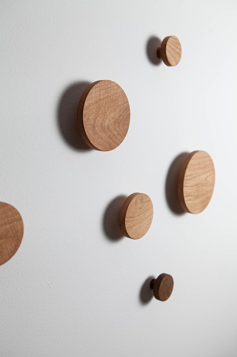 May include: Five wooden wall hooks in various sizes, mounted on a white wall. The hooks are round and have a natural wood finish.