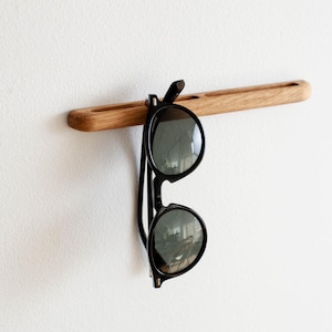May include: A wooden wall-mounted hook with a pair of black sunglasses hanging from it.