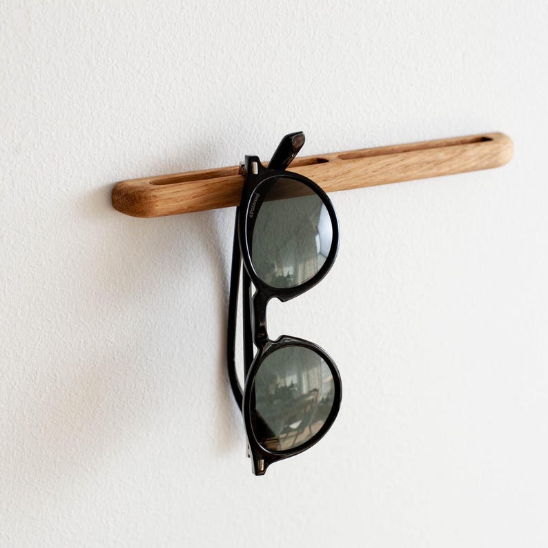 May include: A wooden wall-mounted hook with a pair of black sunglasses hanging from it.