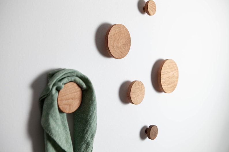 May include: Six wooden wall hooks in various sizes, mounted on a white wall. A green scarf is hanging on one of the hooks.