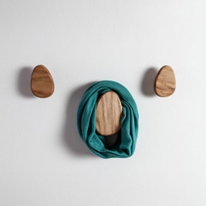 Pu&ograve; includere: Due ganci da parete in legno a forma di uovo, con una sciarpa blu-verde appesa a uno dei ganci.