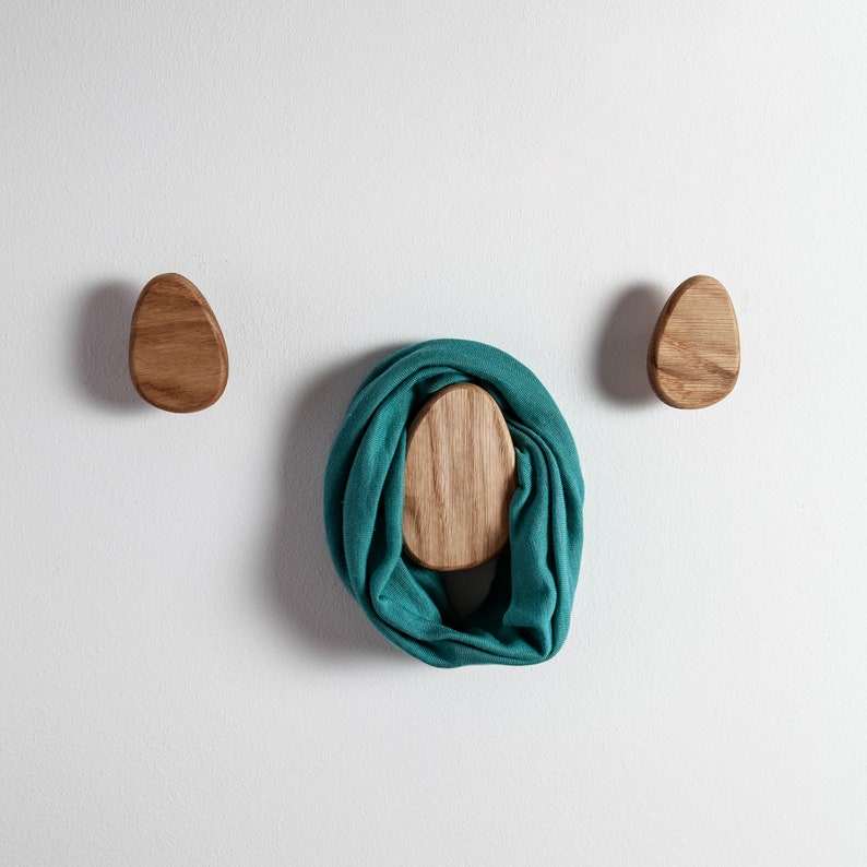 Pu&ograve; includere: Due ganci da parete in legno a forma di uovo, con una sciarpa blu-verde appesa a uno dei ganci.