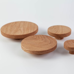 May include: Four wooden knobs of varying sizes, all round and made of light brown wood. The knobs are arranged in a row, with the largest knob on the left and the smallest knob on the right.