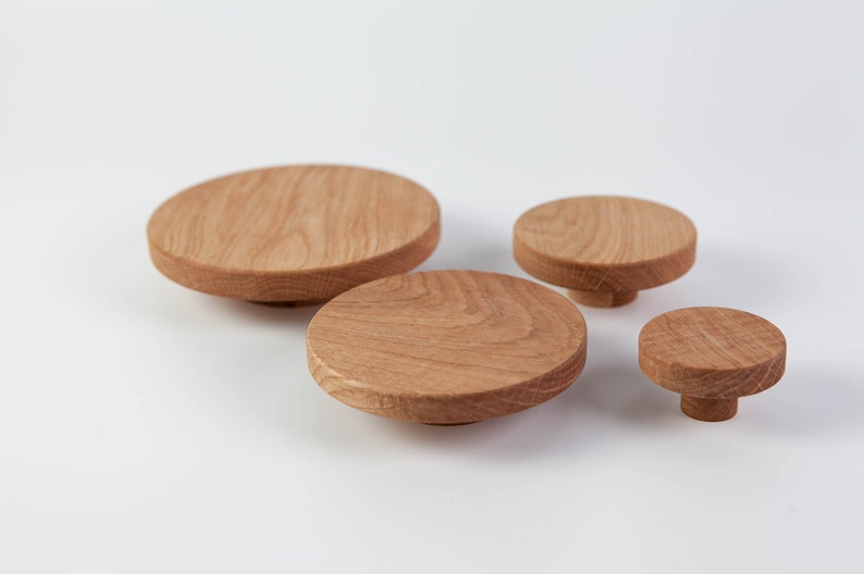 May include: Four wooden knobs of varying sizes, all round and made of light brown wood. The knobs are arranged in a row, with the largest knob on the left and the smallest knob on the right.