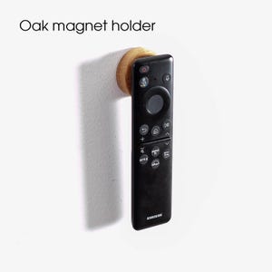 Könnte beinhalten: Ein magnetischer Holzhalter mit einer daran befestigten schwarzen Fernbedienung. Die Fernbedienung hat ein Samsung-Logo und mehrere Tasten, darunter Netflix, Disney+ und Lautstärketasten.