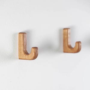 May include: Two wooden hooks mounted on a white wall. The hooks are shaped like the letter "J" and are a light brown color.