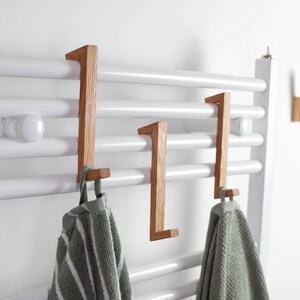 Könnte beinhalten: Holzhandtuchhaken an einem weißen Handtuchhalter. Die Haken sind aus hellbraunem Holz gefertigt und passen über die Stangen des Halters. Zwei grün-weiß gestreifte Handtücher hängen an den Haken.