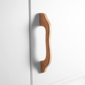 Könnte beinhalten: Ein hellbrauner Holzschrankgriff mit geschwungenem Design ist an einer weißen Schranktür befestigt. Der Griff besteht aus hellem Holz und hat eine glatte, natürliche Oberfläche. Der Griff ist vertikal montiert.