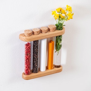 Peut inclure: Un présentoir à épices en bois avec cinq tubes en verre, chacun rempli d'épices et d'herbes différentes. Le présentoir contient également un petit bouquet de fleurs jaunes. Le présentoir est en bois clair et possède un bouchon en liège pour chaque tube.
