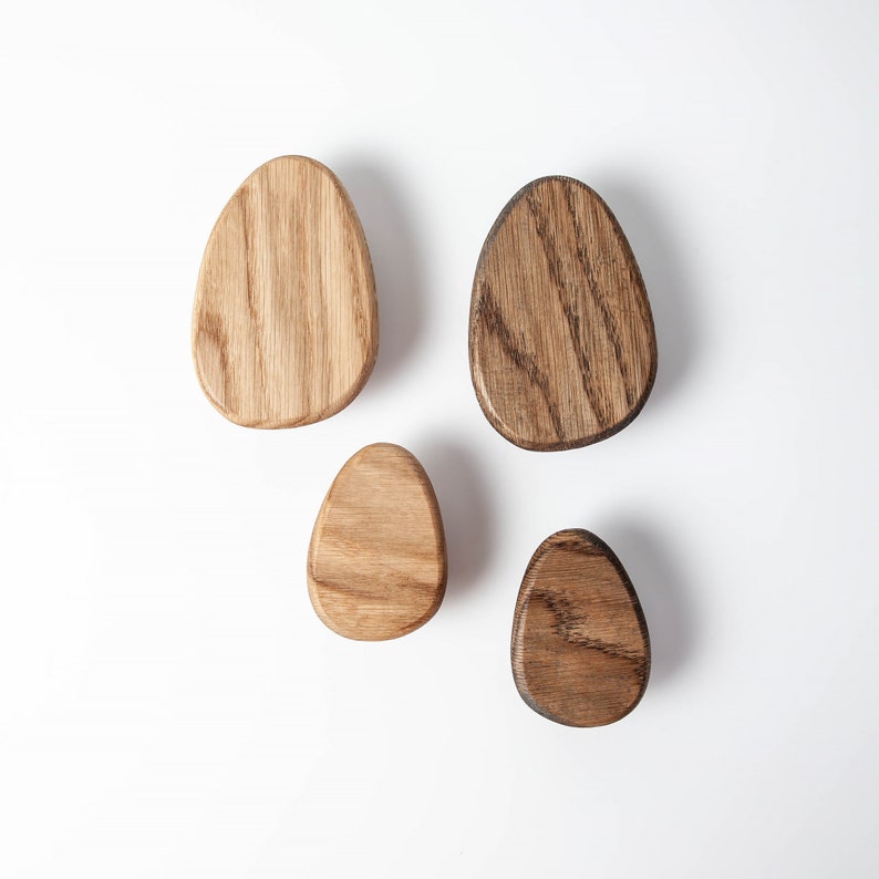 Pu&ograve; includere: Quattro ganci da parete in legno a forma di uovo. I ganci sono realizzati in legno naturale e hanno una finitura marrone chiaro e marrone scuro.