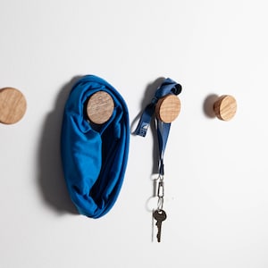 May include: Four wooden knobs mounted on a white wall. A blue scarf is hanging from one knob, and a blue lanyard with a key is hanging from another knob.