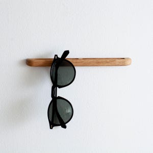 May include: A wooden wall-mounted shelf with a pair of black sunglasses hanging from it.