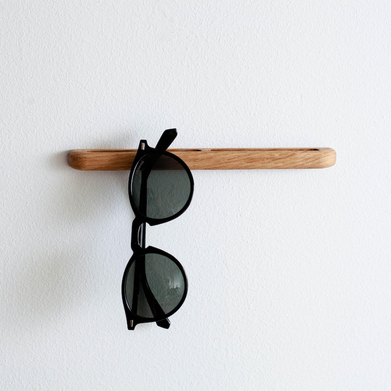 May include: A wooden wall-mounted shelf with a pair of black sunglasses hanging from it.
