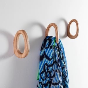 Könnte beinhalten: Drei ovale Wandhaken aus Holz mit abgerundeten Kanten. An einem Haken hängt ein Schal mit blauem und grünem Muster.