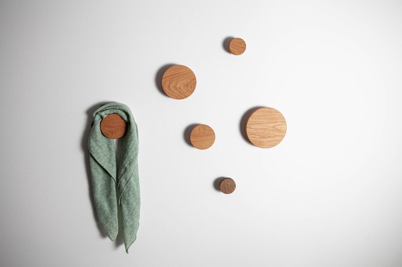 May include: Five wooden wall hooks in various sizes, with a green scarf hanging on one of the larger hooks.
