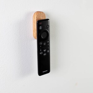 May include: A black remote control with a wooden wall mount. The remote has a circular navigation button and buttons for Netflix, Disney+, and other streaming services.