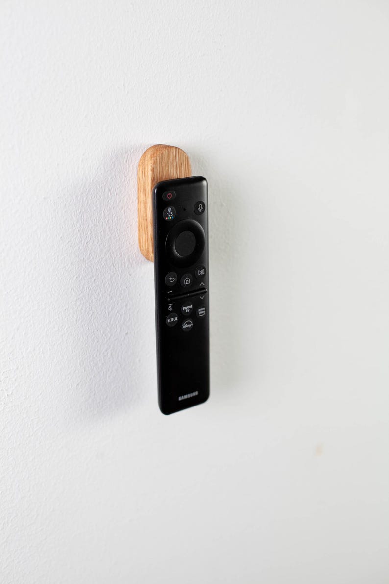 May include: A black remote control with a wooden wall mount. The remote has a circular navigation button and buttons for Netflix, Disney+, and other streaming services.