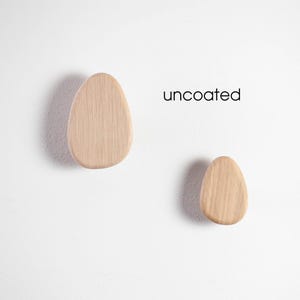 May include: Two wooden hooks in the shape of a rounded oval, mounted on a white wall. The text "uncoated" is printed on the wall.