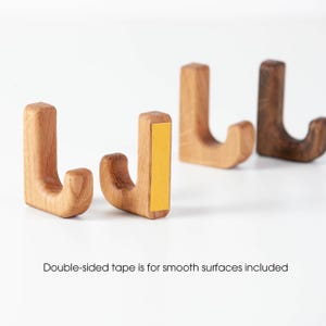 May include: Four wooden hooks with a J-shape design. The hooks are made of natural wood and have a light brown color. Double-sided tape is included for smooth surfaces.