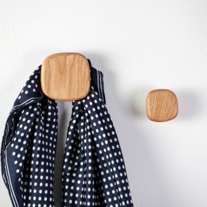 Op de afbeelding: Twee houten wandhaken met een afgeronde vierkante vorm. Aan één haak hangt een blauwe en witte stippen sjaal.
