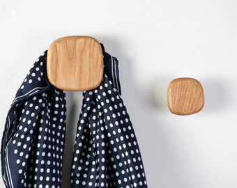 May include: Two wooden wall hooks with a rounded square shape. One hook has a blue and white polka dot scarf hanging from it.