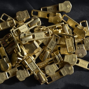 May include: A pile of gold-colored metal zipper pulls with the text "YKK" on them.