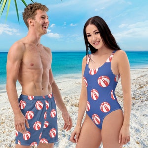 Puede incluir: Una pareja lleva trajes de baño a juego con un patrón de pelota de playa roja y blanca sobre un fondo azul. El hombre lleva pantalones cortos de baño y la mujer lleva un traje de baño de una pieza.