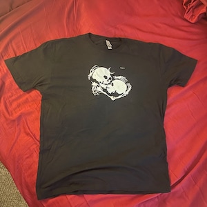 May include: Black t-shirt with a white graphic of two skeletons embracing. The skeletons are kissing and have a crescent moon above them.