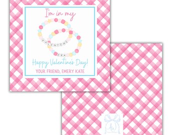 May include: Pink and white gingham patterned card with a blue border. The card features a drawing of two bracelets with the words "I'm in my Valentine Era" and "Happy Valentine's Day! Your friend, Emery Kate".