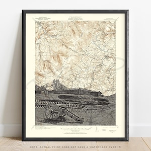 May include: Framed vintage map print with a black frame. The map features detailed topographical lines and a depiction of a Civil War battlefield, including a cannon and fortifications. The color palette is primarily sepia tones, giving it a historical aesthetic.
