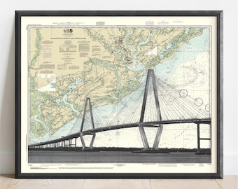 May include: Framed print of a nautical chart depicting Charleston Harbor and Approaches. The map features a detailed illustration of the area, including the Ravenel Bridge. The print is in shades of beige, green, and blue, with black text and a black frame.